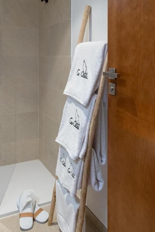 Toallas blancas con logotipo cuelgan de una escalera de madera en un baño, cerca de la ducha y la puerta abierta.