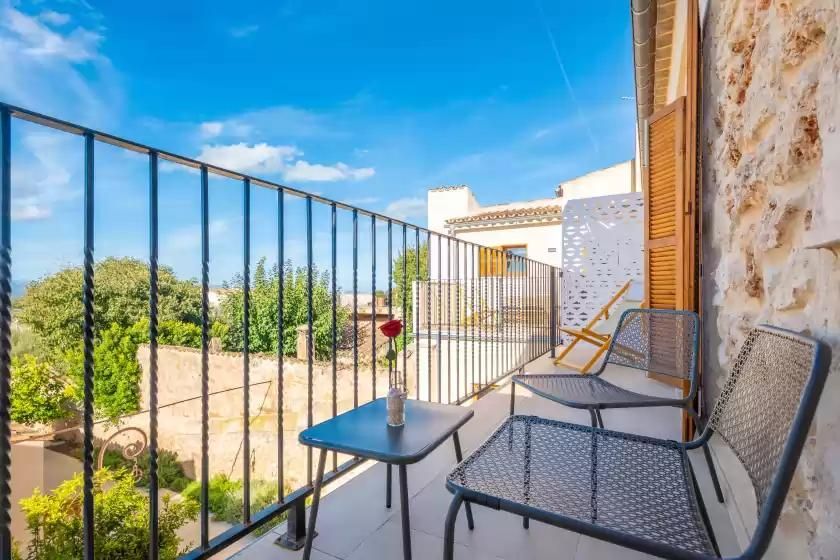 Balcón con sillas y mesa, con vistas a los árboles y edificios contra un cielo azul.