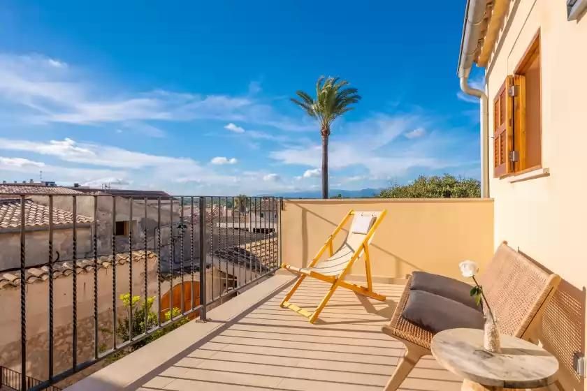 Balcón con asientos, palmera y cielo azul.