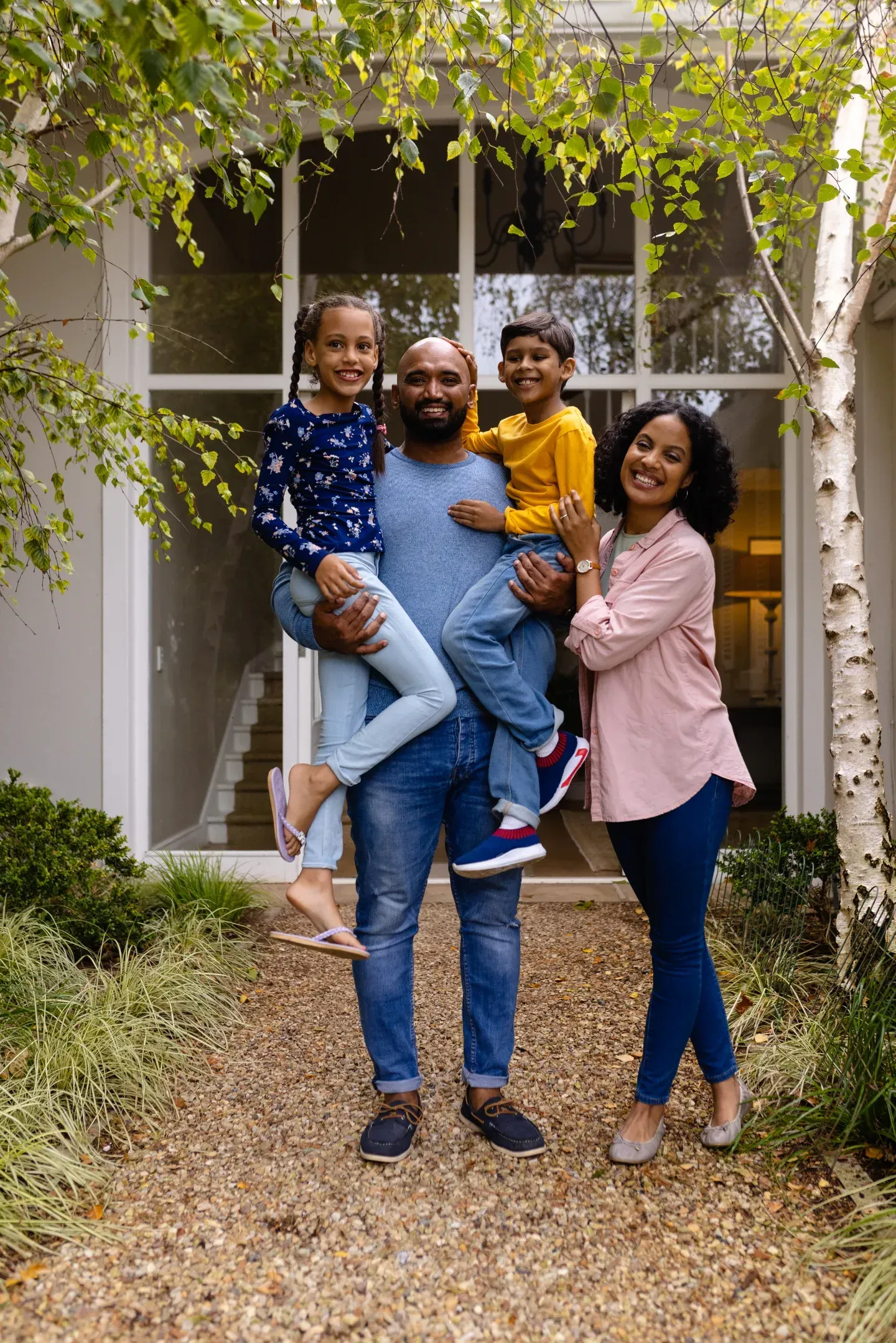 Family of four poses in front of a house with the father holding the children.