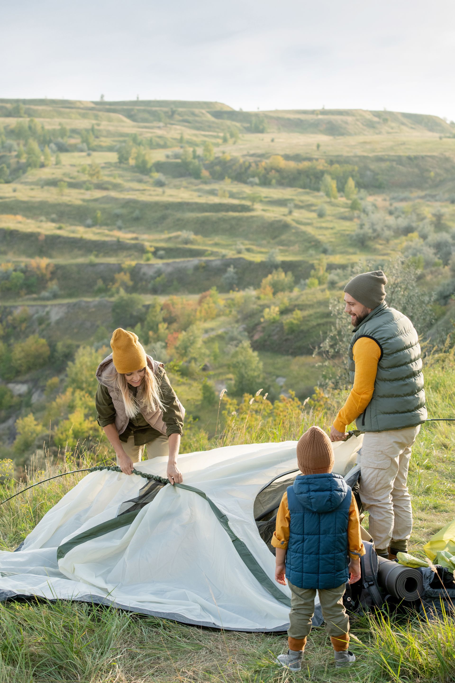 Family setting up a tent on a hillside, with mother, father, and child.