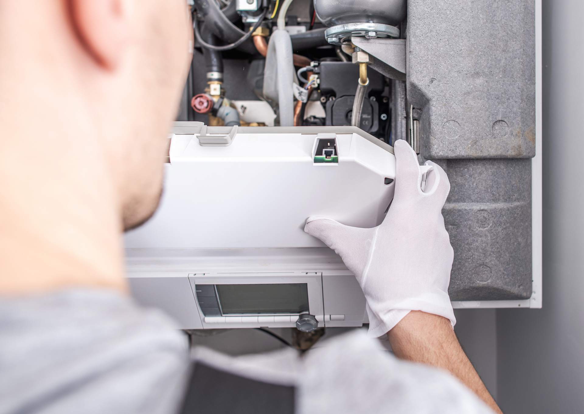 A man wearing white gloves is working on a boiler.