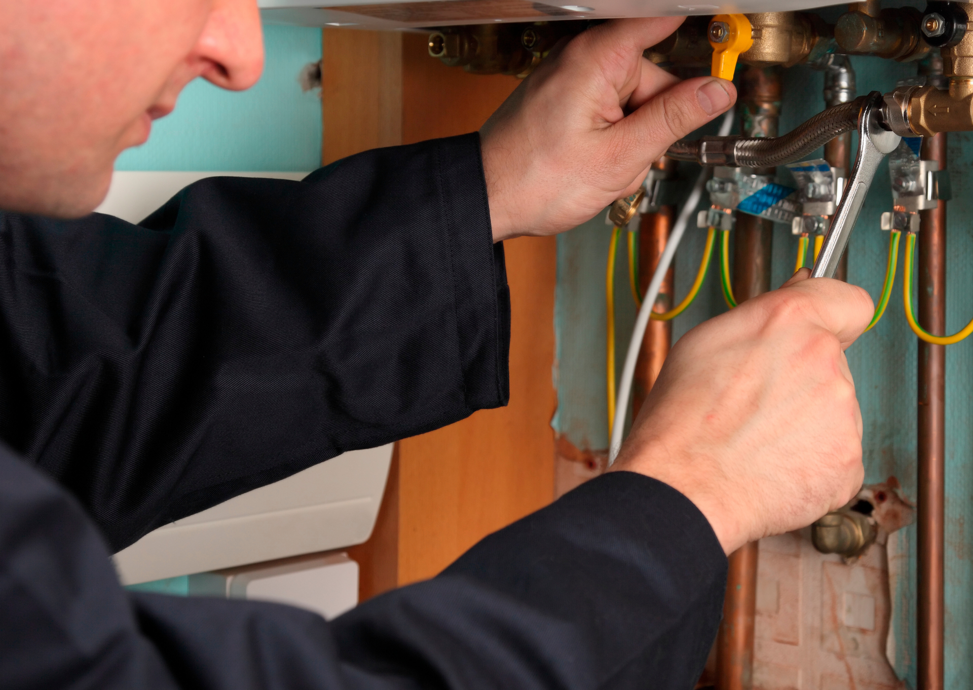 A man is fixing a water heater with a wrench