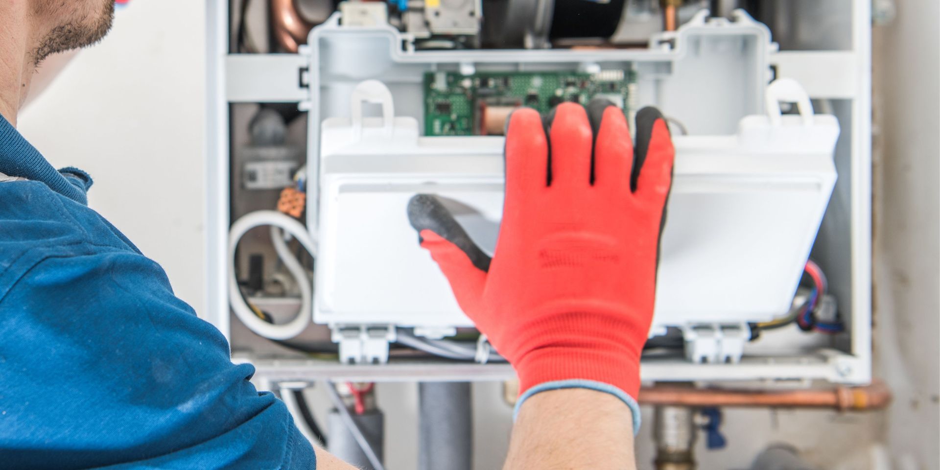 A man wearing red gloves is working on a boiler.