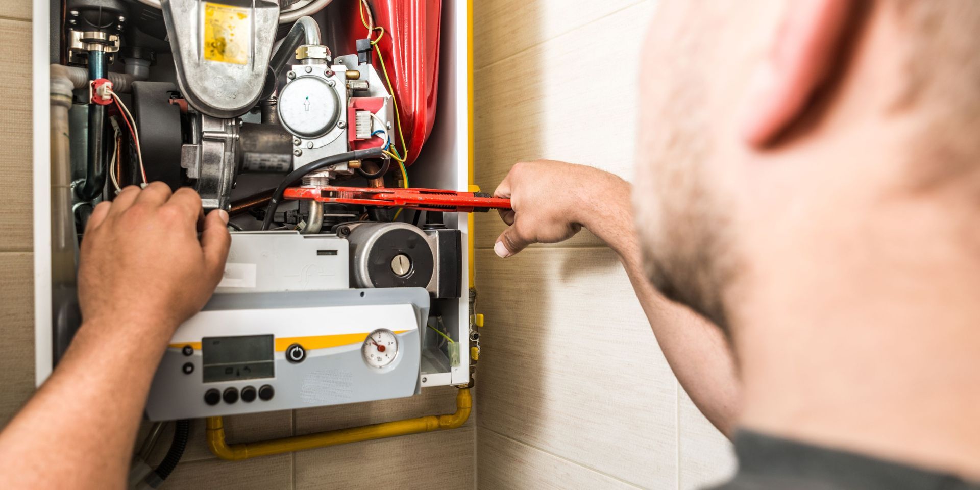 A man is fixing a boiler with a wrench.