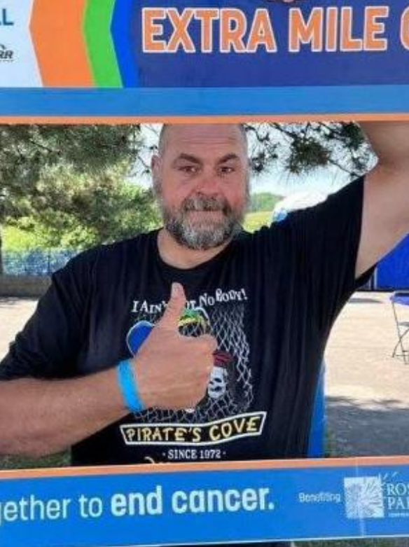A man giving a thumbs up in front of a sign that says extra mile