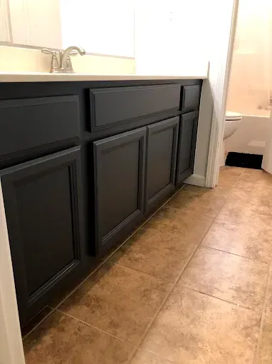Dark gray bathroom vanity with countertop, tan floor tiles, and a glimpse of a toilet.