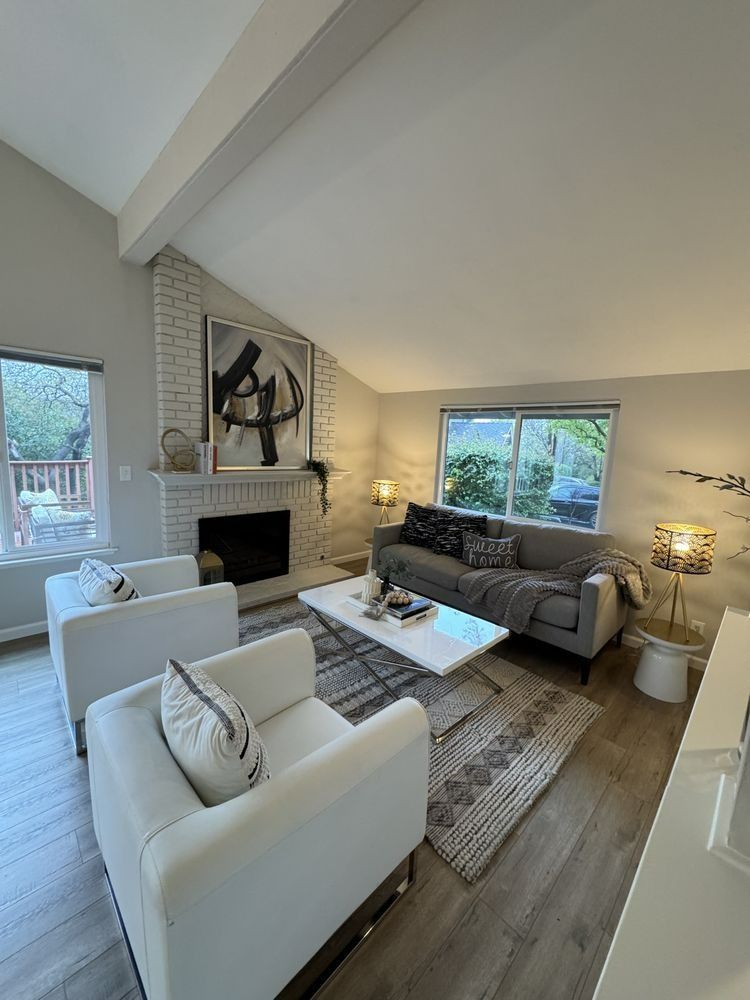 Living room with white brick fireplace, gray sofa, white chairs, and modern art.