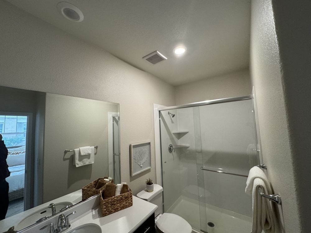 Bathroom with a shower, toilet, sink, mirror, and towel rack. Light gray walls.