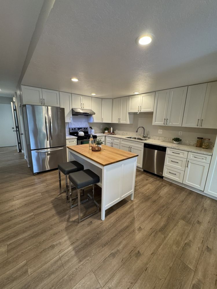 Modern white kitchen with stainless steel appliances, a wooden island, and gray flooring.