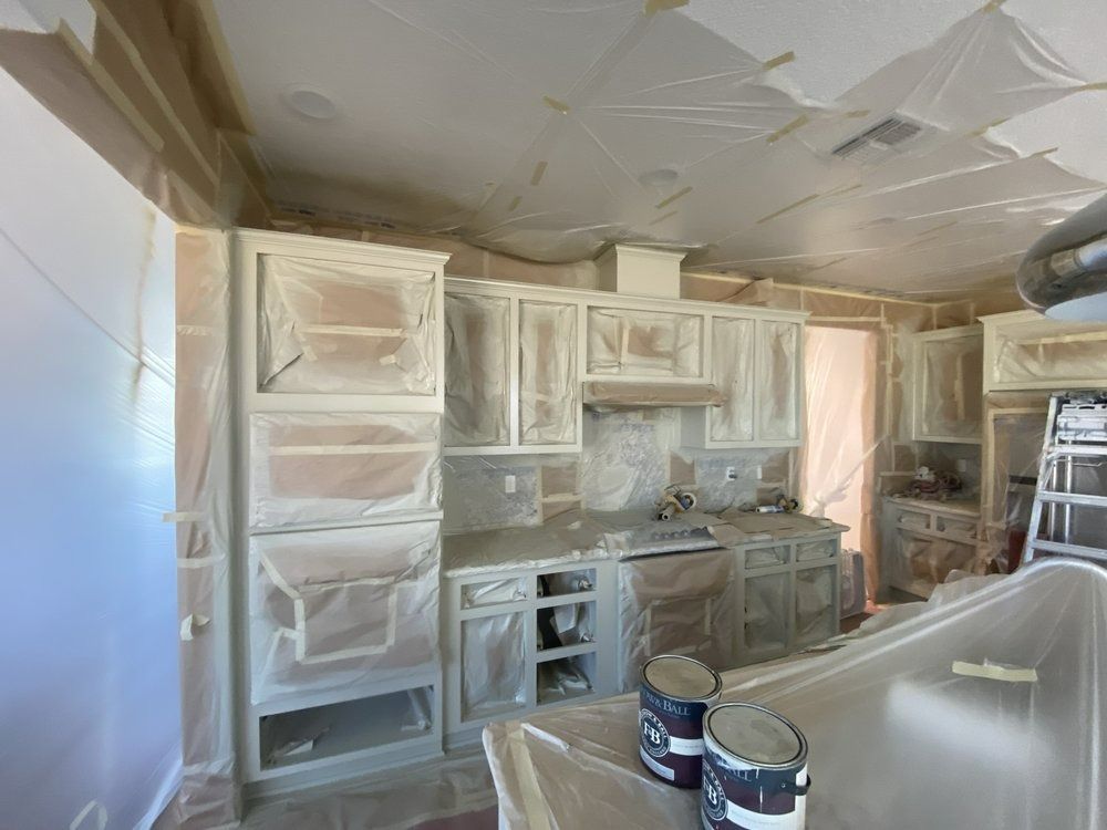 Kitchen cabinets and ceiling covered with plastic sheeting, being painted white during renovation.