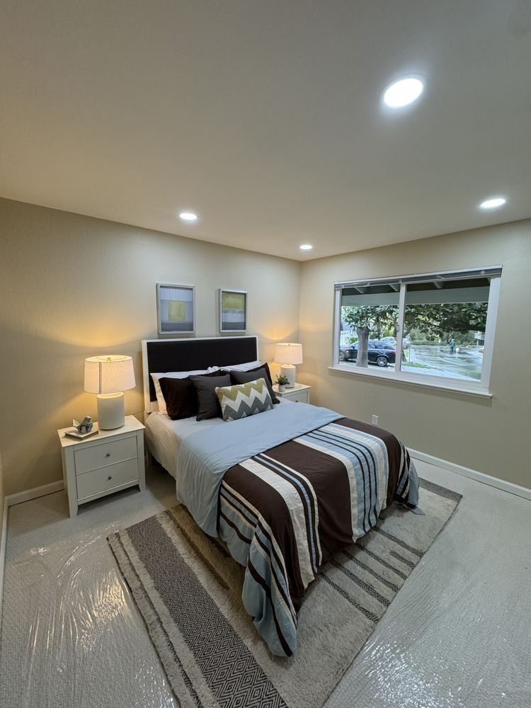 Bedroom with bed, nightstands, and window; neutral walls, brown and blue bedding.