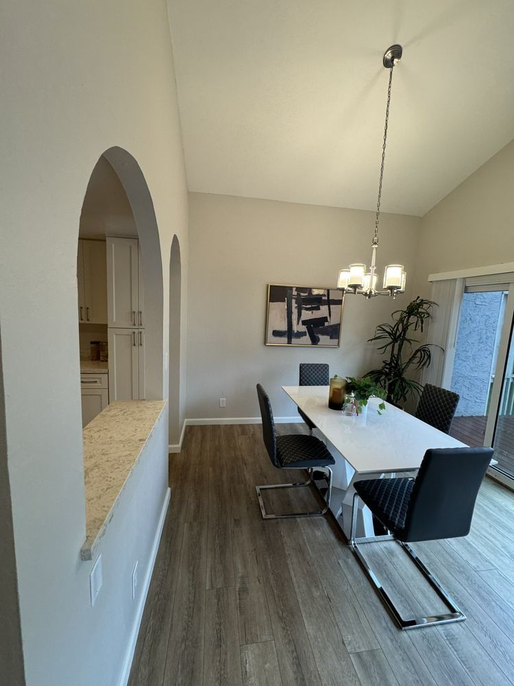 Dining area with white table, black chairs, and contemporary art; connects to kitchen via arched opening.
