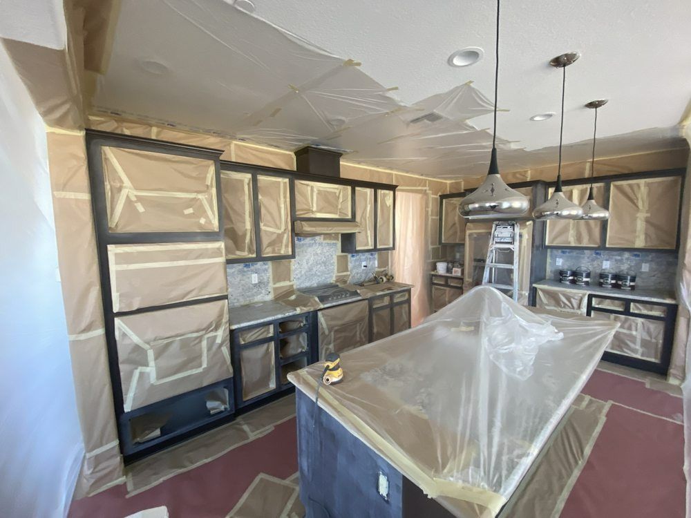Kitchen renovation in progress: Cabinets and island covered in protective material. Brown, gray, and silver tones.