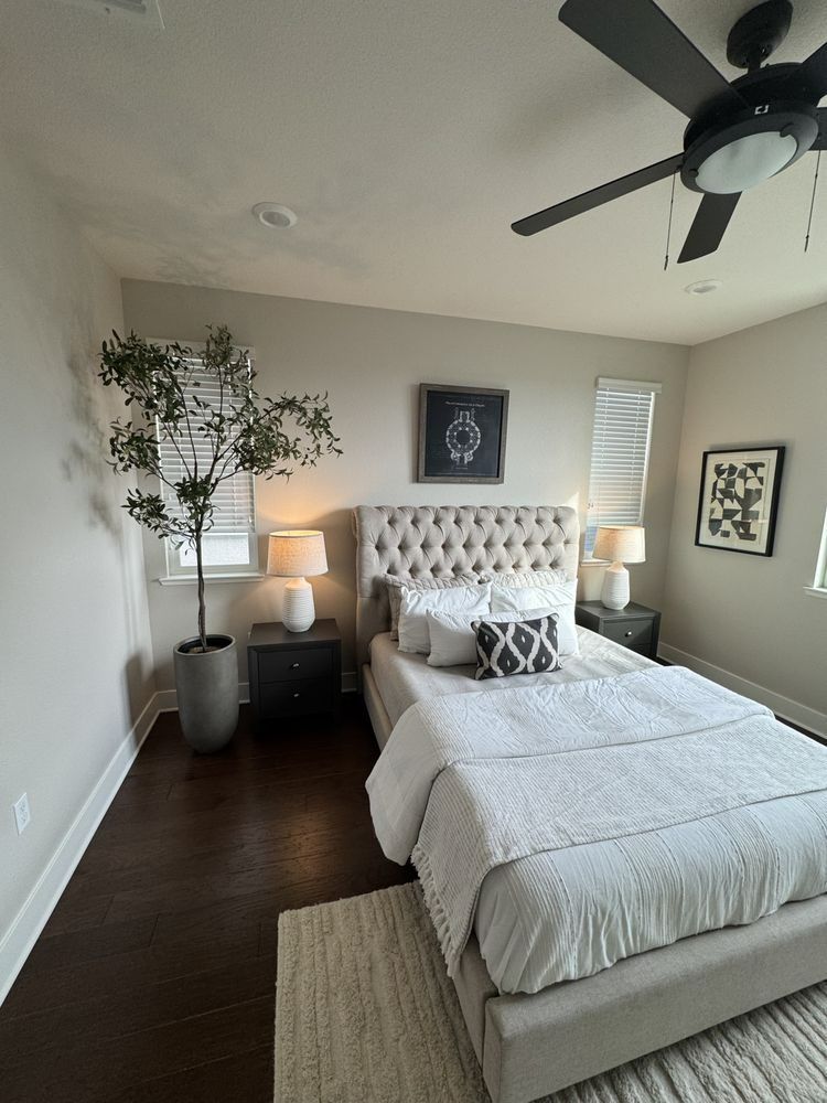 Bedroom with tufted headboard, dark wood floor, ceiling fan, potted tree, neutral color palette.