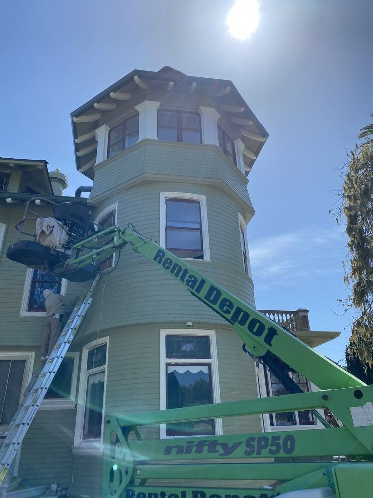 Green building with tower being painted from a Rental Depot lift on a sunny day.