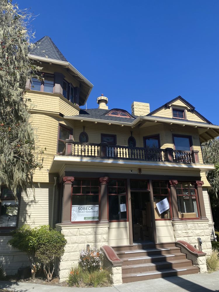 Yellow Victorian house with a tower and a balcony, under a clear blue sky.