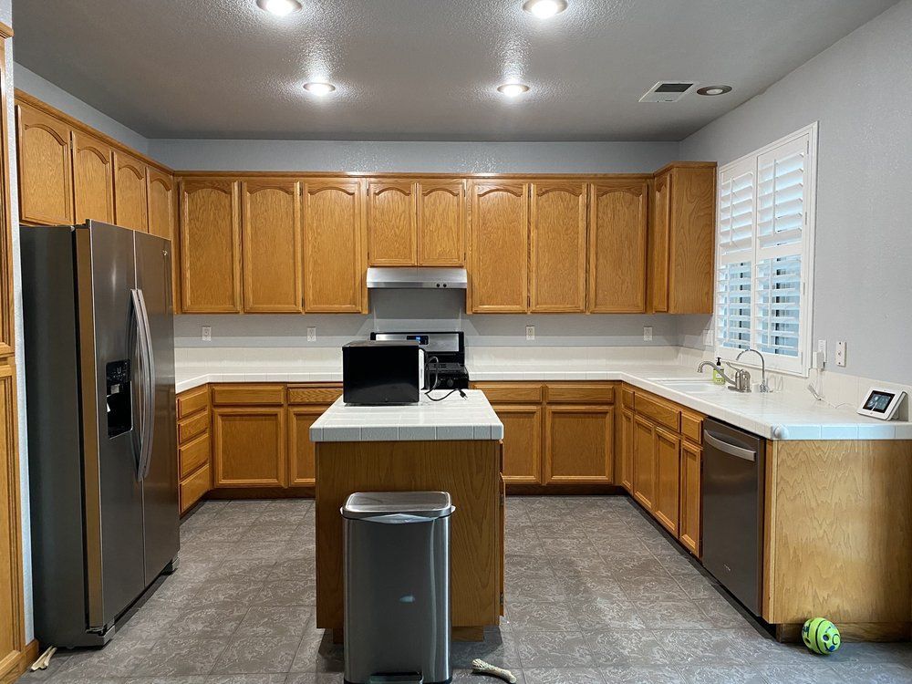 Kitchen with wood cabinets, stainless steel appliances, white countertops, and a gray floor.