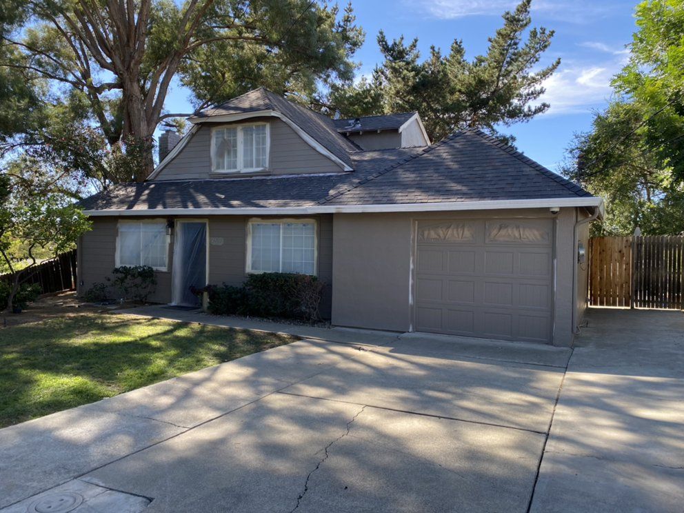 Gray house with a dark roof, two-car garage, and dormer window; driveway and lawn in front.
