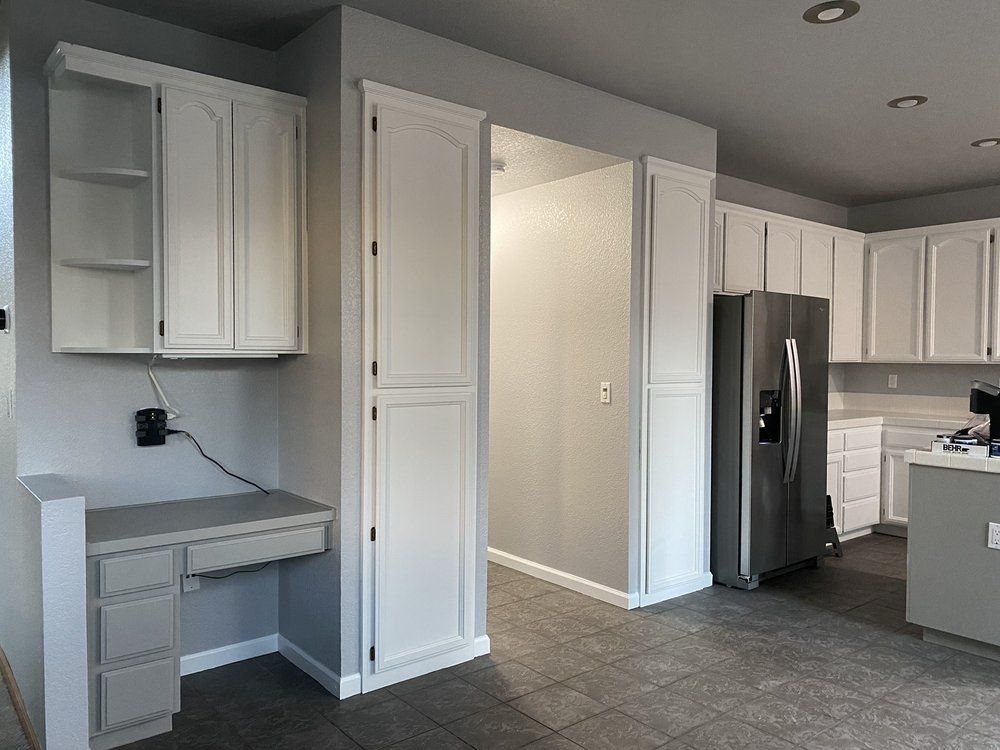 Kitchen with white cabinets, gray walls, built-in desk, and stainless steel refrigerator.