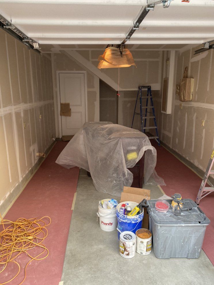Garage interior under construction; drywall, tools, and a covered item in the center. Pink floor protection.