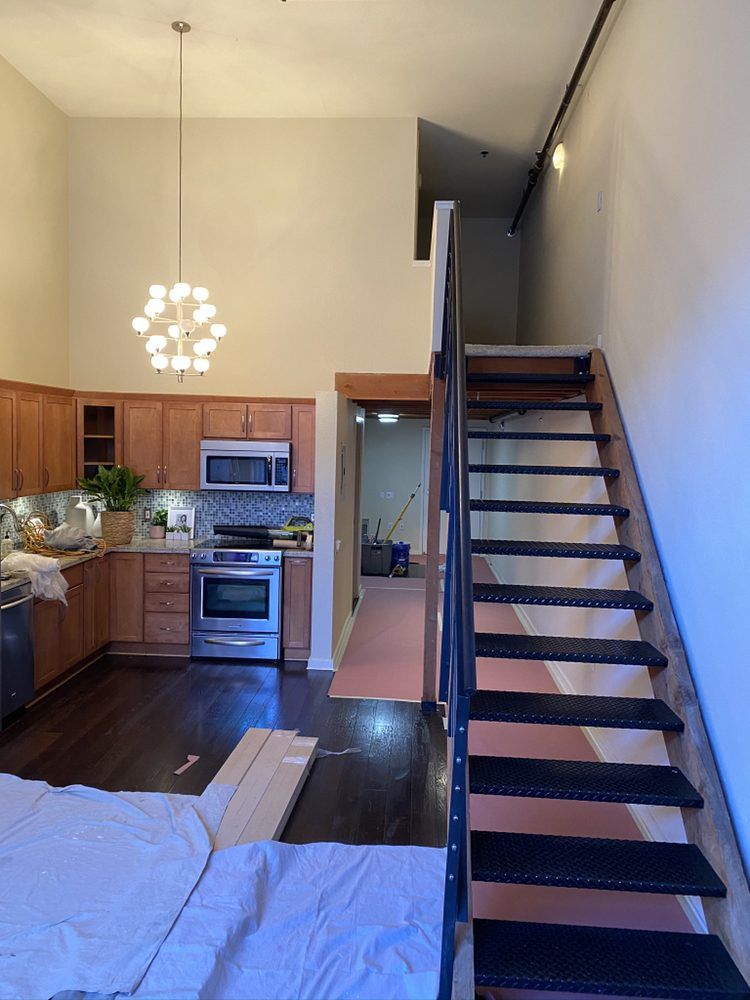 Loft kitchen with stairs. Light wood cabinets, stainless appliances, dark floors, stairs lead up.