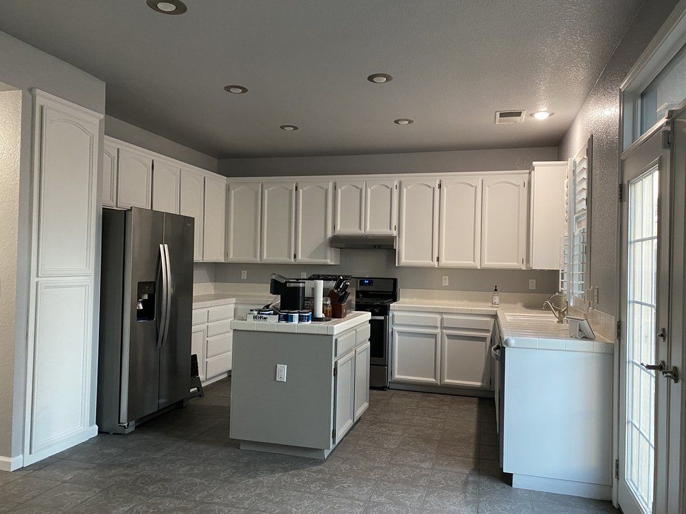 White kitchen cabinets and island with stainless steel appliances. Gray walls and flooring.