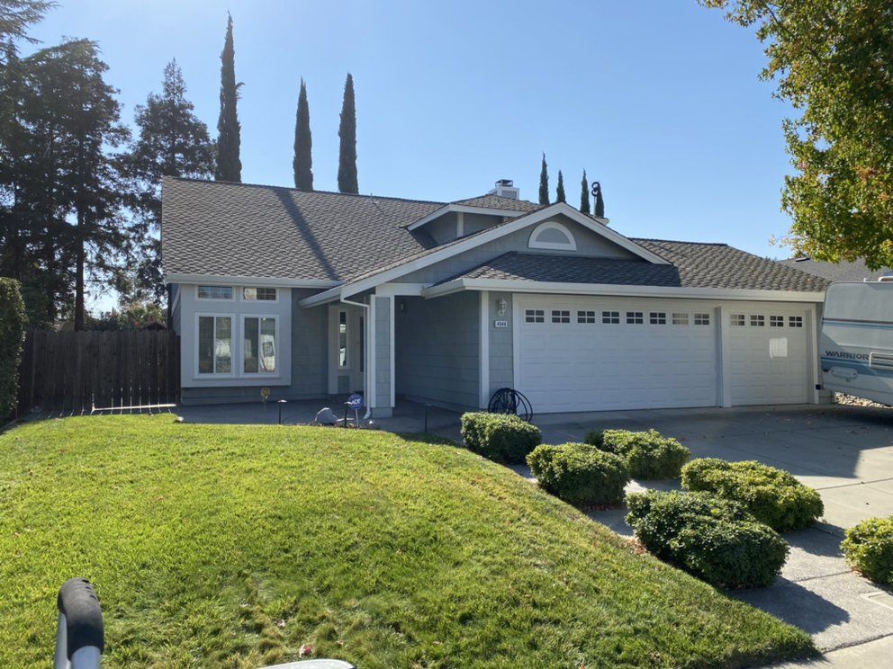 Light blue house with a white garage door, green lawn, and blue sky.