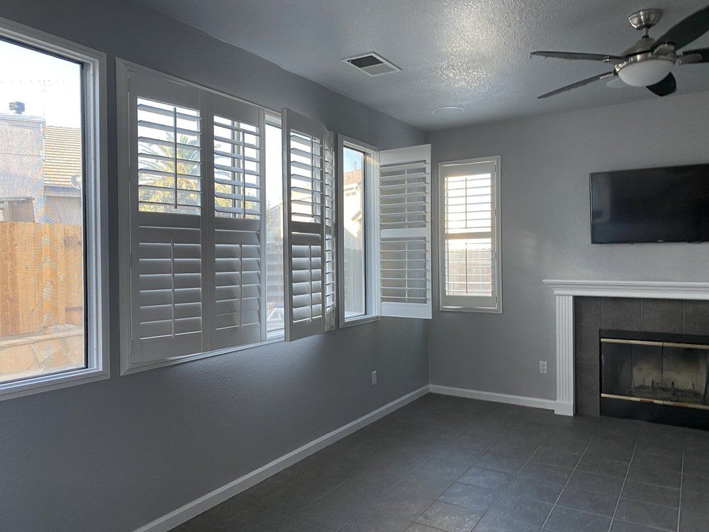 Empty living room with gray walls, window shutters, fireplace, and mounted TV.