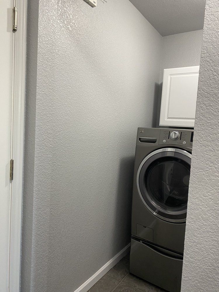 Laundry room with gray washer and dryer, white cabinet, and light gray textured walls.
