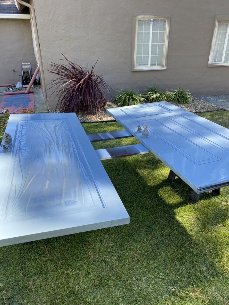 Two gray doors, freshly painted, lie on the grass outside. A house is in the background.