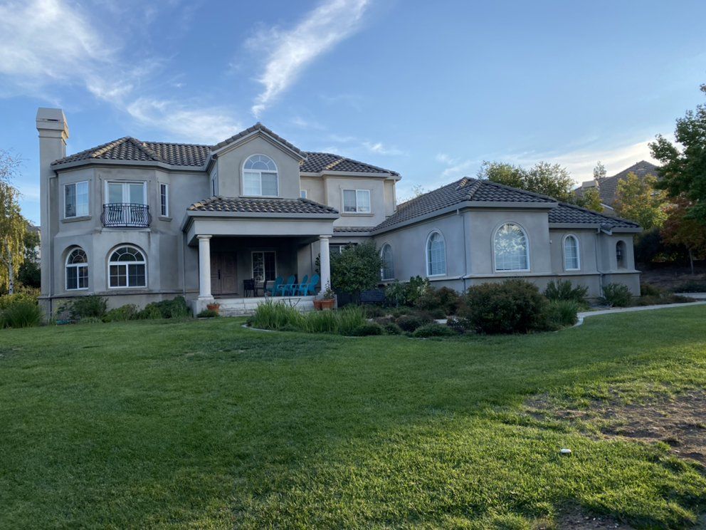 Large two-story stucco house with a tile roof and green lawn on a sunny day.