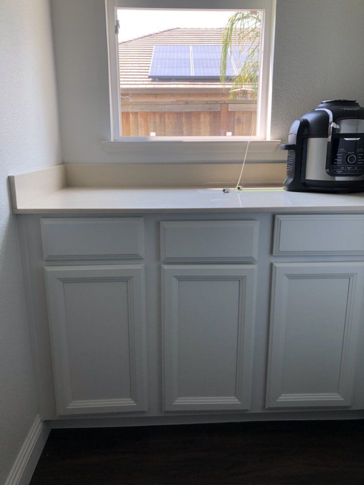 White kitchen cabinets beneath a window, with a countertop and coffee maker.