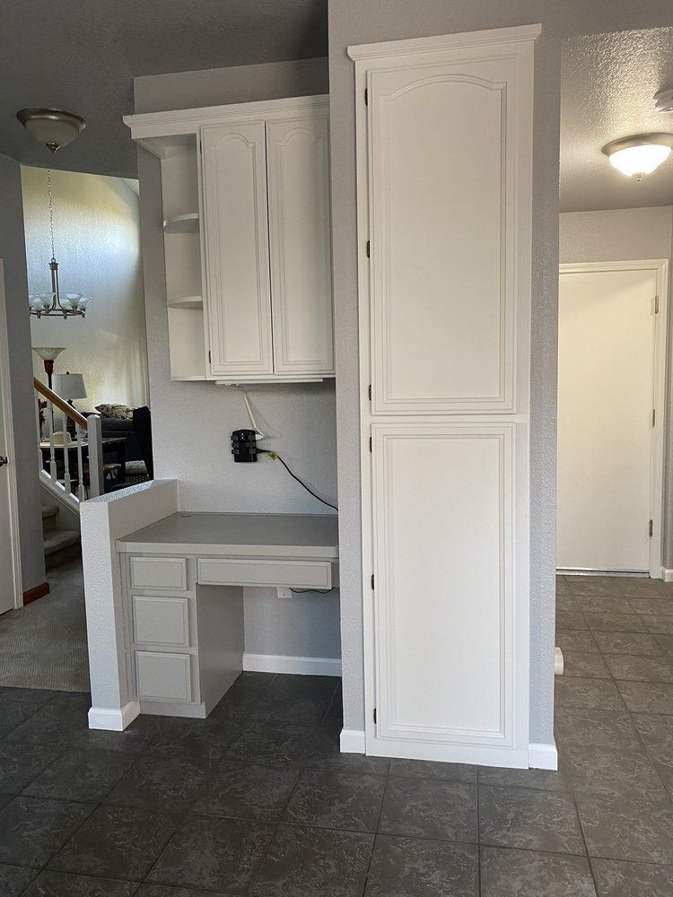Built-in white cabinets, desk, and pantry on a gray wall in a home.