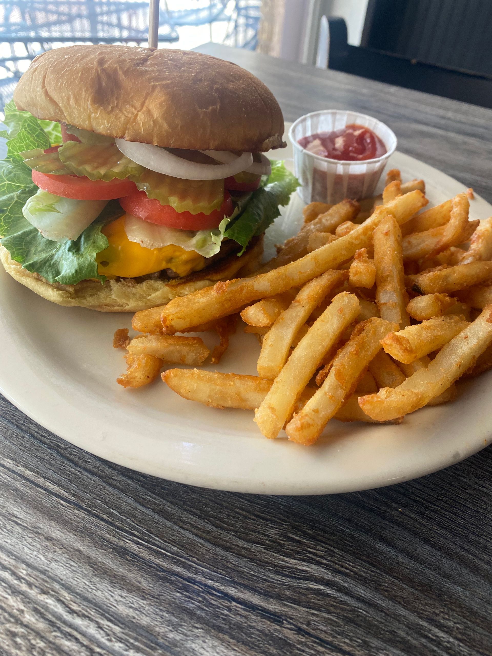 Cheeseburger with fries and ketchup on a plate, on a wooden table.