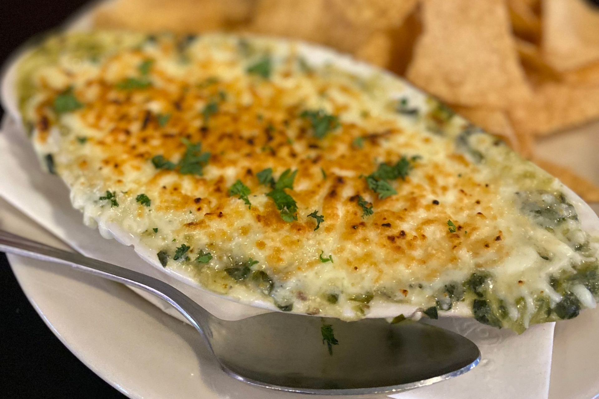Spinach and artichoke dip with chips, garnished with parsley on a white plate.