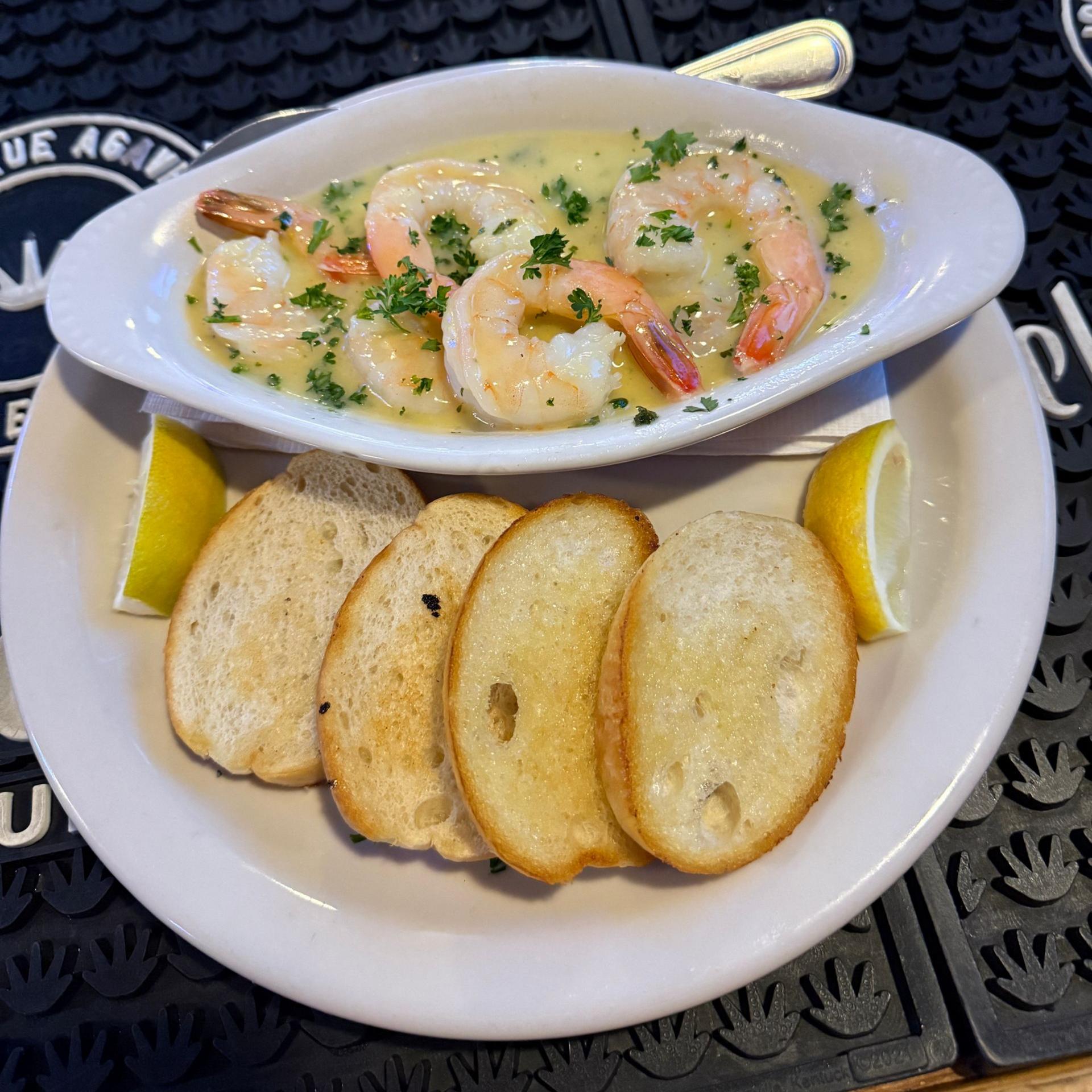 Shrimp scampi in a white dish with bread slices and lemon wedges on a plate.