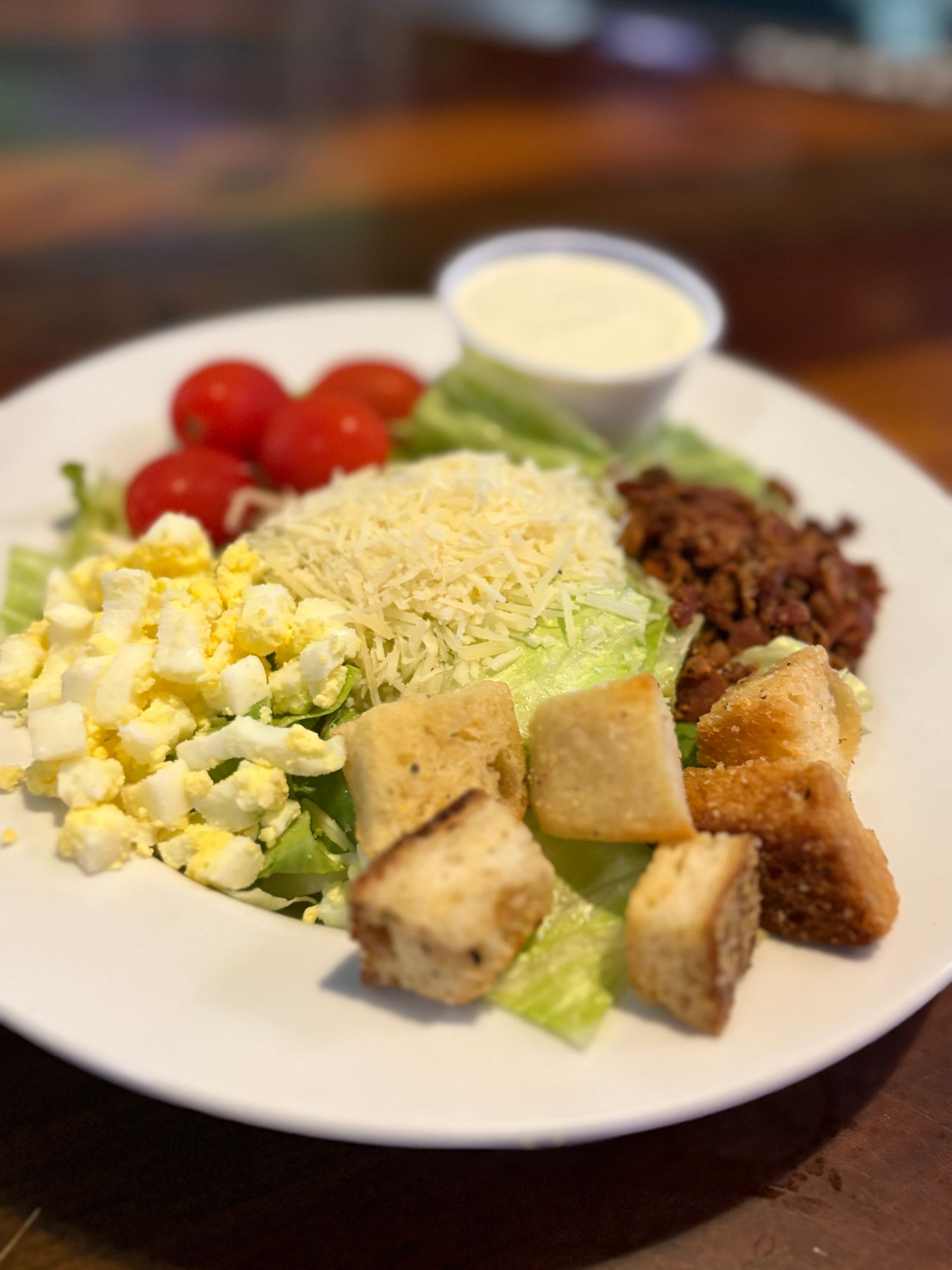 Salad with tomatoes, egg, croutons, shredded cheese, and meat; a side of white dressing.
