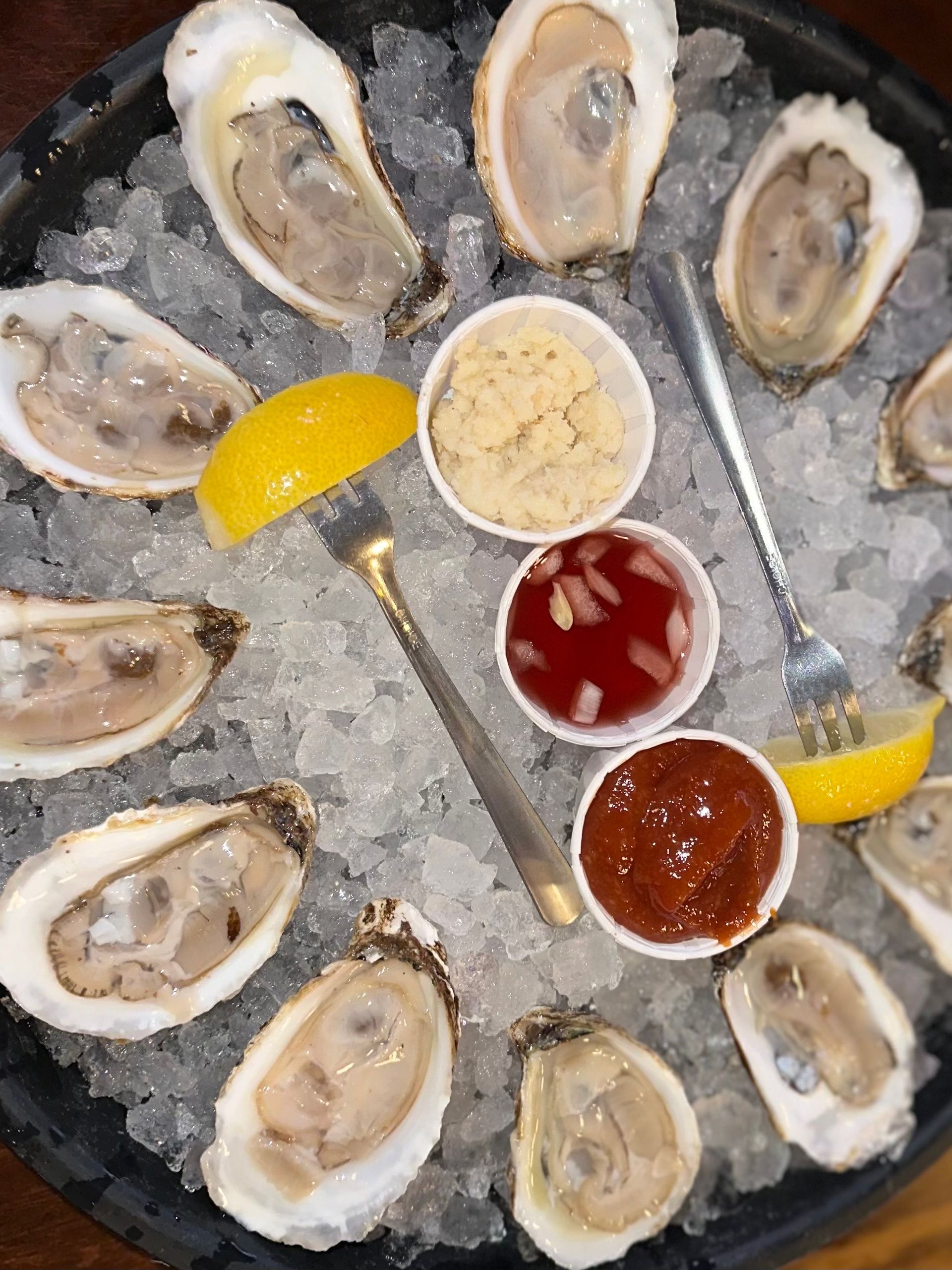 Oysters on ice with lemon, cocktail sauce, and horseradish in a round tray.