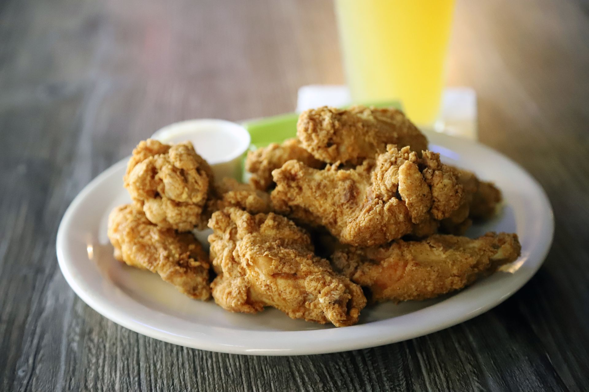 Plate of fried chicken wings, celery, and dipping sauce. A glass of beer is visible in the background.