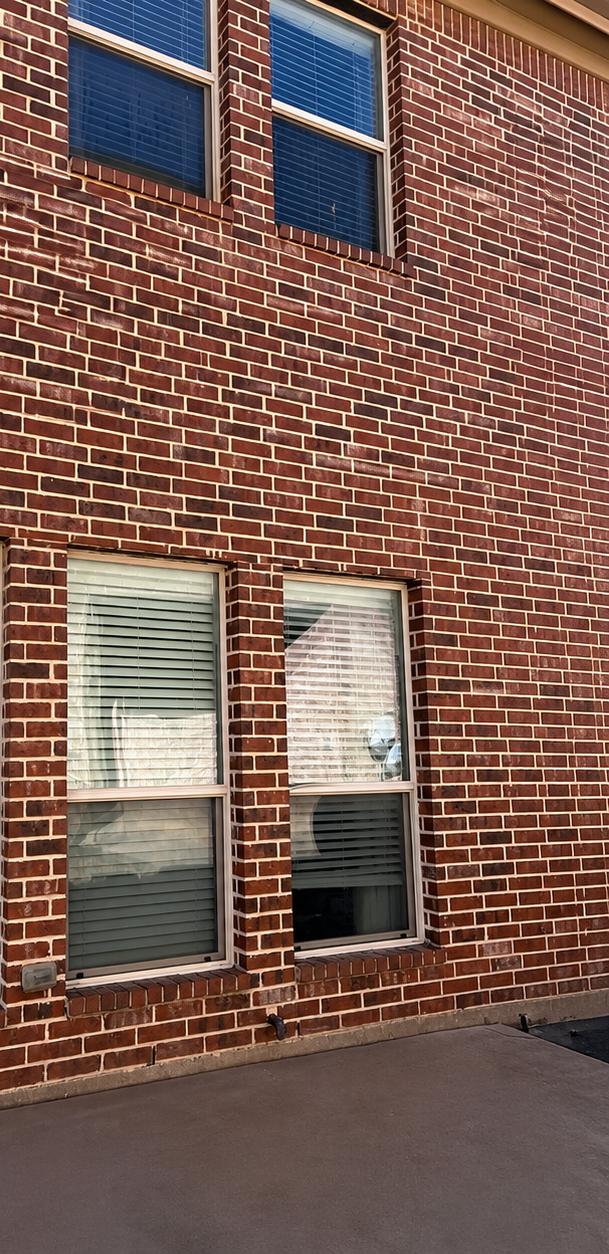 Red brick building wall with two windows and a small doorway or panel near the sidewalk.