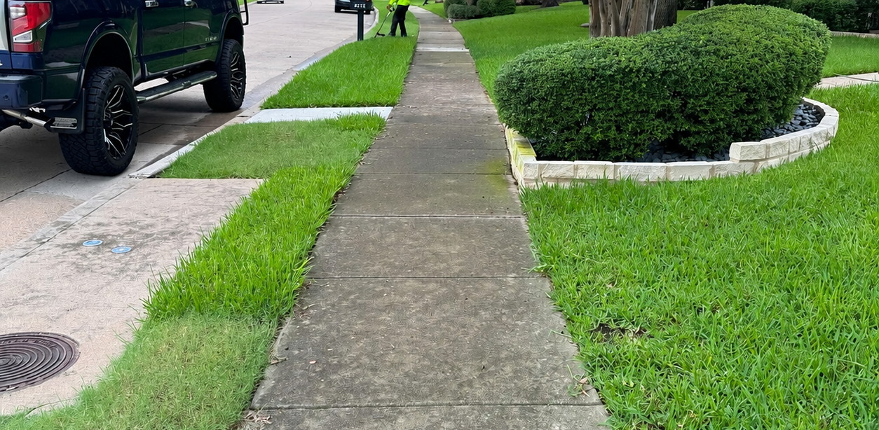 Residential sidewalk beside a green lawn and trimmed hedge, with a black truck parked at left