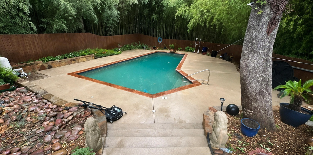 Backyard swimming pool with tan deck, stone steps, and surrounding trees and plants