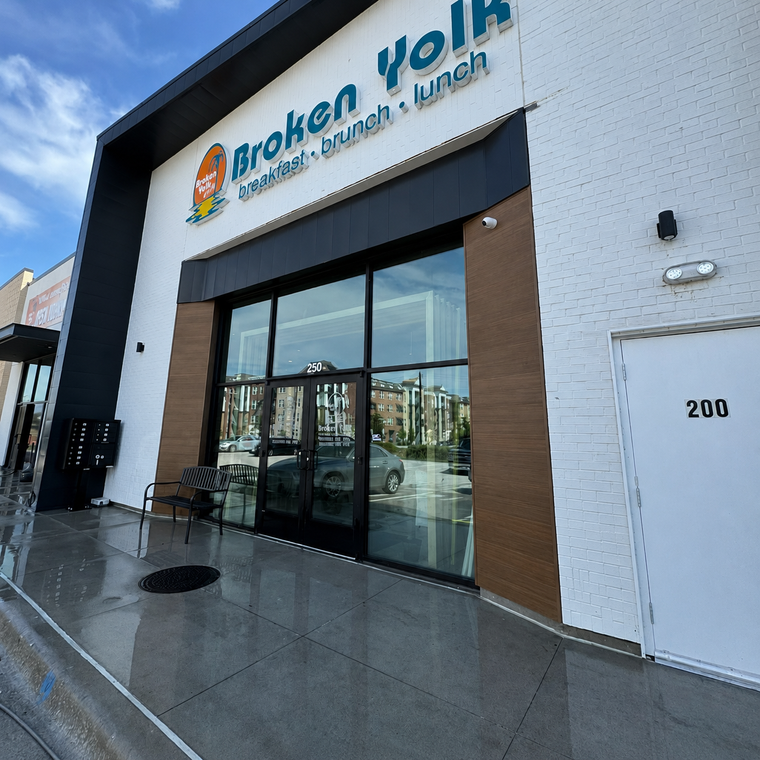 Worker pressure-washing a commercial building facade on a wet sidewalk