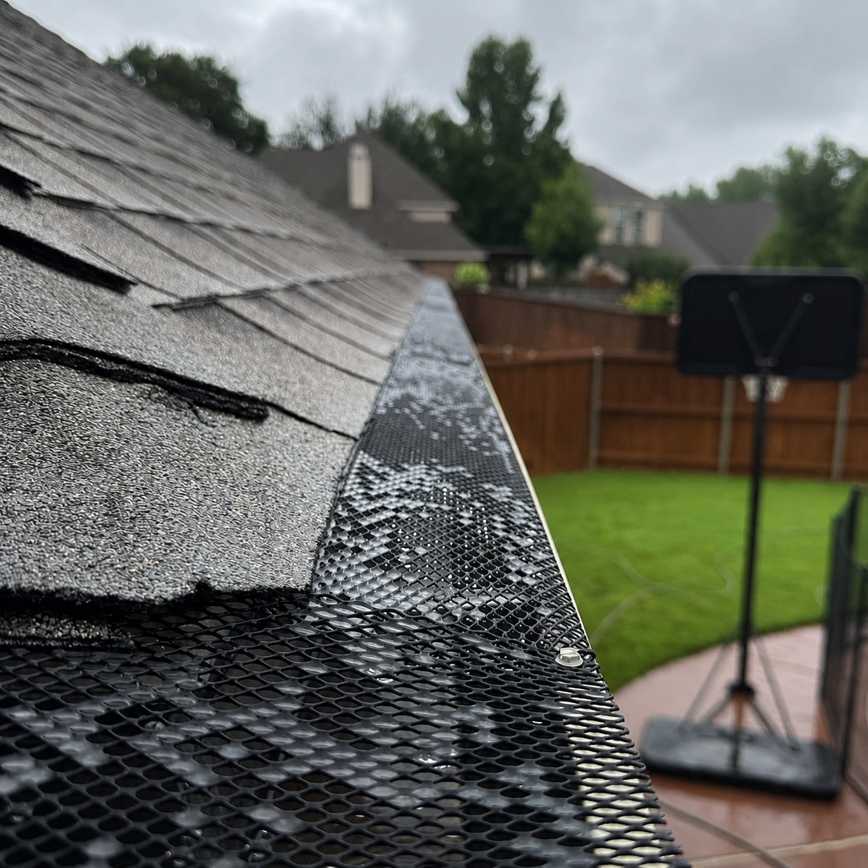 Close-up of a roof gutter guard along a dark shingled roof edge