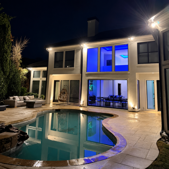 Modern two-story house with lit windows and a blue-lit backyard pool at night