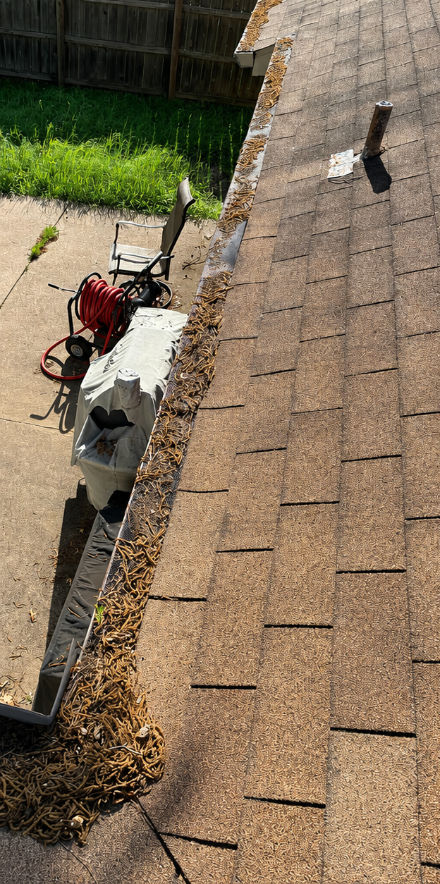 Roofing tools and materials beside a shingled roof edge, with a person working below.