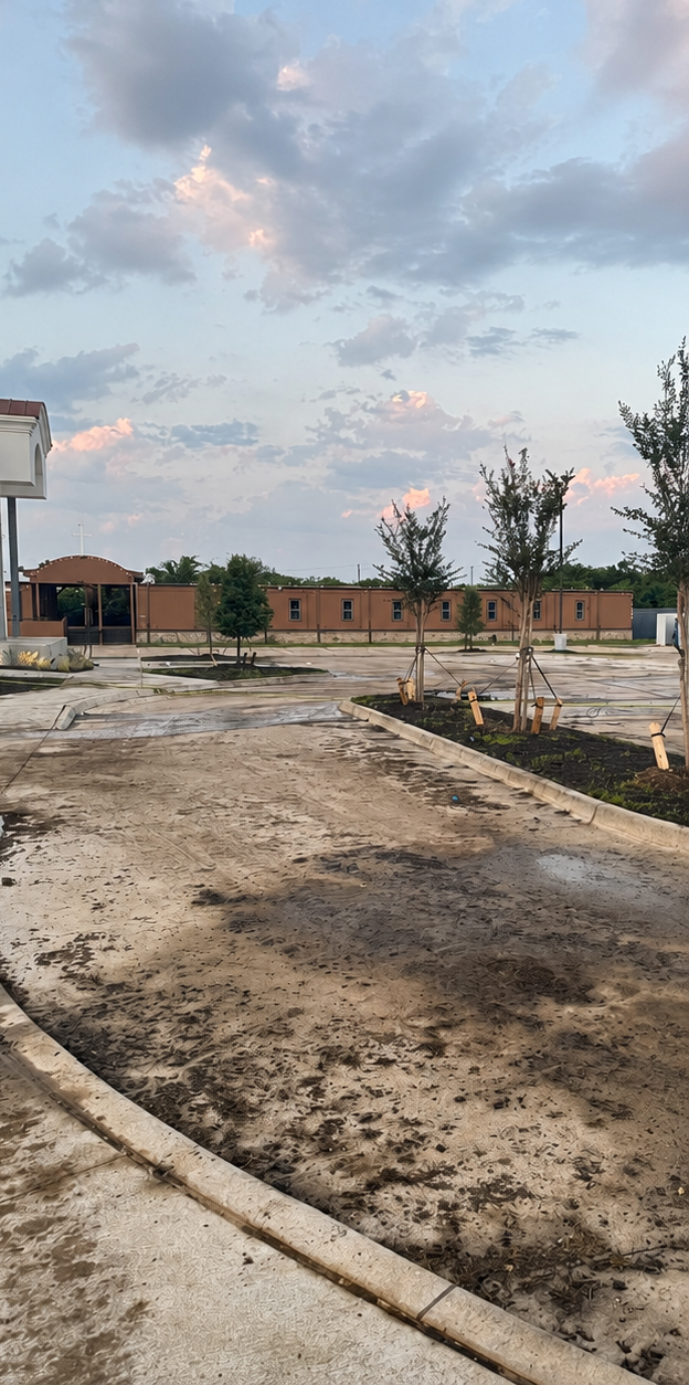 Mud path beside a fenced lot with brick buildings and cloudy sky at dusk