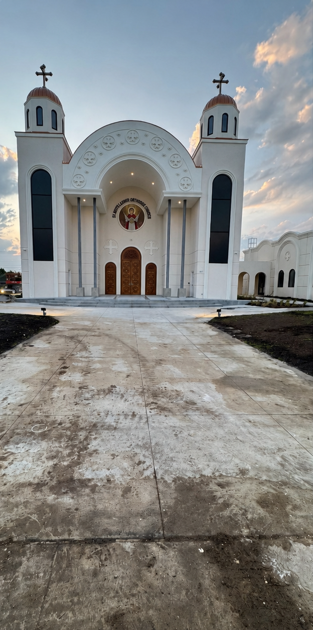 White church facade with two bell towers, arched entrance, and a cloudy sky at dusk