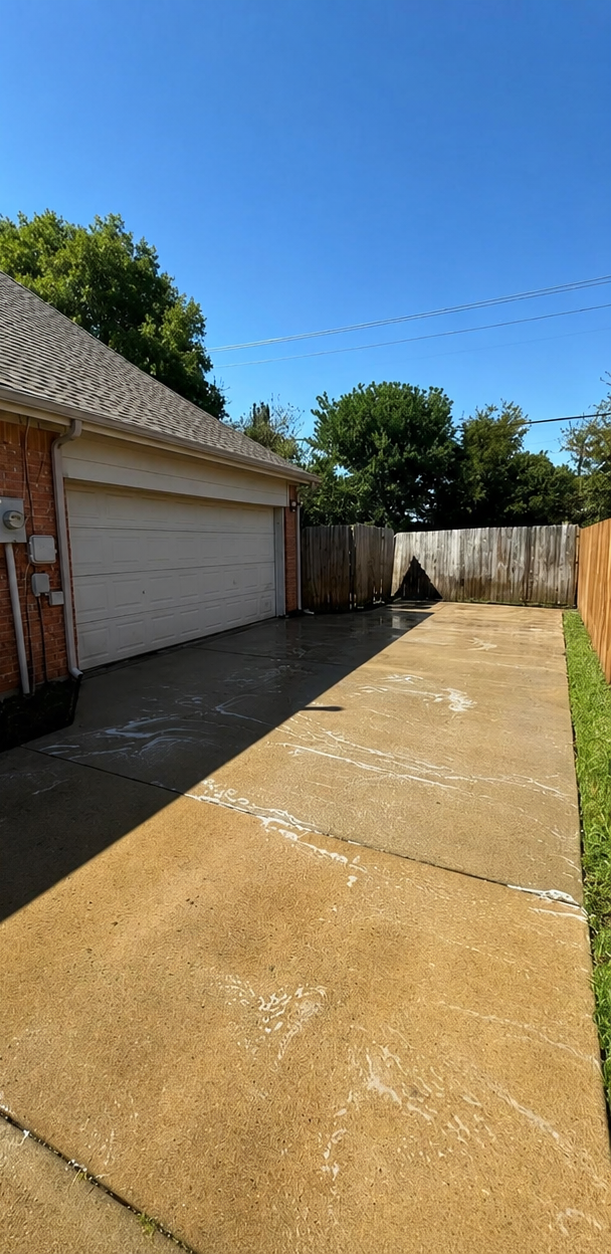 Sunny residential driveway beside a garage, with a concrete path and wooden fence under a blue sky